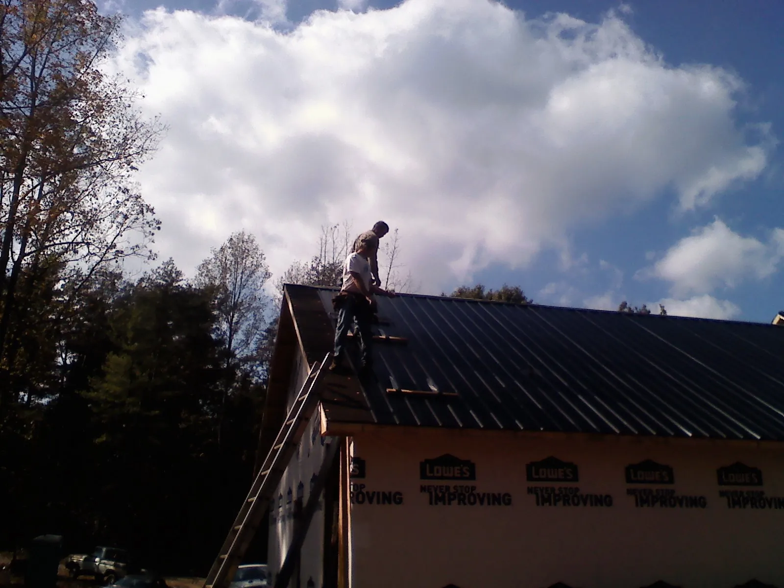 Roofer fastening dark metal panels high against a cloudy sky, from a Roof Inspection job in Warrenton